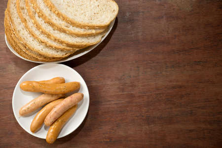 slice brown cut plain bread with dish of Sausage on white dish wood backgroundの写真素材