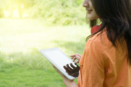 beautiful asian woman stand on green grass meadow nature park use tablet for education conceptの写真素材
