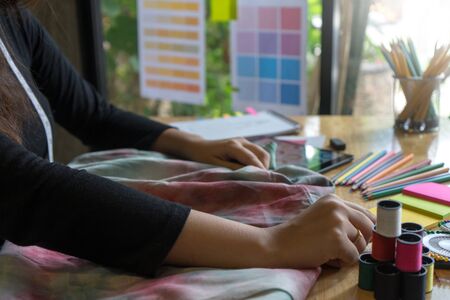 young fashion designer work with fabric cloth on the wood table near the green tree out door