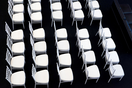 row of empty white chair on black carpet in hall room  top view