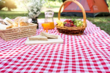 Blur picnic bread croissant basket with fruit on  red white cloth and vase flower with jar of orange...