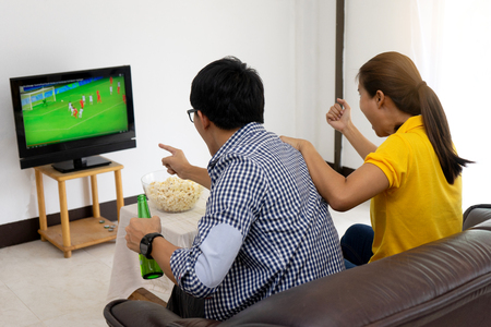 man and woman watch Football match on tv broadcast program cheer and existing together in familyの写真素材