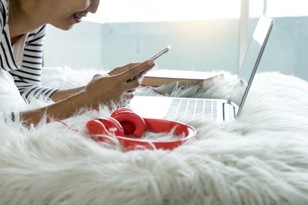 smile girl lying on the bed play her smartphone and laptop computer with red headphone