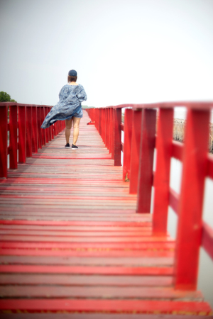 woman walking on the wood red bridge near the seaの写真素材