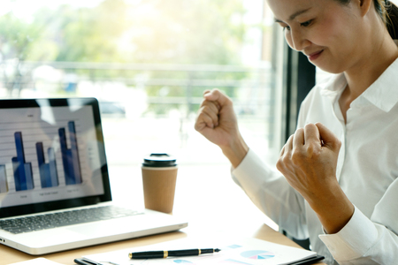 freelance worker work in the coffee shop ,on table have computer laptop and marketing paper graph chart with calculator.  She feel so happy and excited.の写真素材