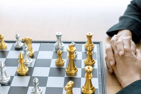 Businessman thinking and hold king chess on his hand,on board of chess game silver and gold color chess are on the tableの写真素材