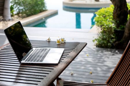 Laptop computer on the wood table near the swimming pool.の写真素材