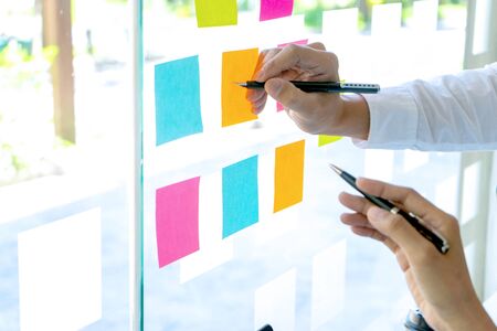 Young businesspeople use their hand point to color sticky note on glass windowの写真素材