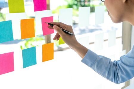 Young businesspeople use their hand point to color sticky note on glass window