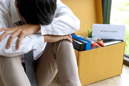 Young worker feel bad and sad, he receive resign note from his boss and company. Sad business man pack his belonging in the box and go back home.の写真素材
