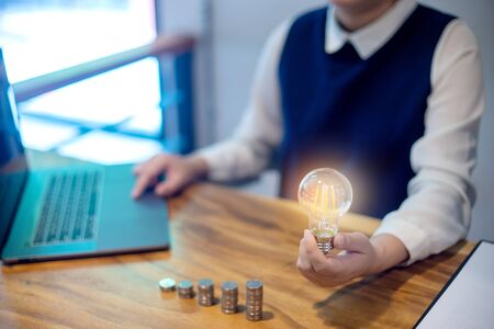 Young woman sit near the computer laptop her hand hold the glass bulb near the group of step coin.の写真素材