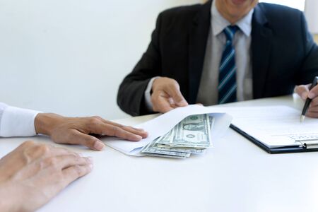 Business man give bribe to the officer under contact paper, concept corruption moneyの写真素材