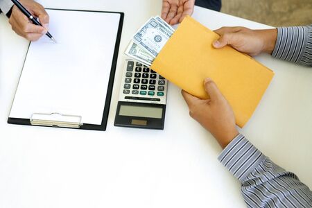 Business man give bribe to the officer under contact paper, concept corruption moneyの写真素材