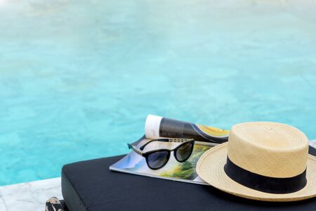 Book and hat on the sun bed near the swimming pool, with tree shadow.の写真素材