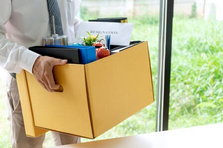 Young worker feel bad and sad, he receive resign note from his boss and company. Sad business man pack his belonging in the box and go back home.の写真素材