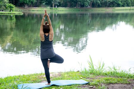Woman more than 50 year old practicing yoga outdoor location near the lake in the park area. enjoy nice day in nature and positive energyの写真素材