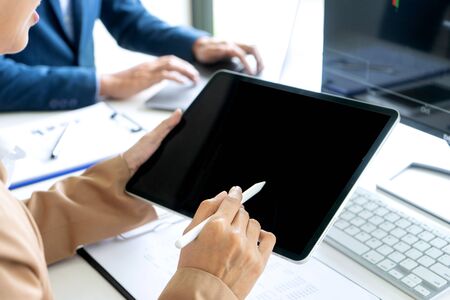 business woman sit at the table looking at tablet and computer laptop in the office , they talking about stock market invest or talk with customer, with  white tablet screenの写真素材