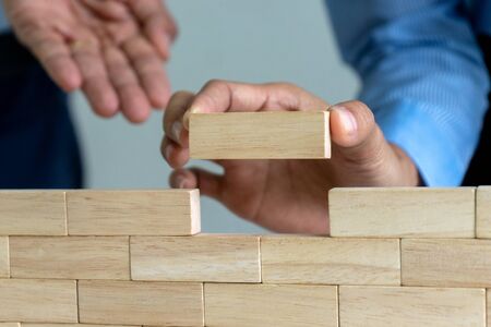 group of  Young businessman try to build wall and tower from wooden brick block go to top of a tower