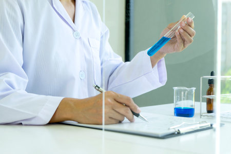 In the chemical laboratory Technician looking at the blue chemical tube on the panorama white...