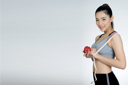 Beautiful sport slender woman with a tape measure and apple in the white background with more copy spaceの写真素材