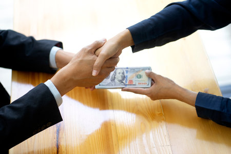 Businessman shake hand with officer and hold the cash in his hand sign to give bribe concept corruptionの写真素材