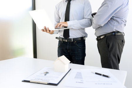 Two businessmen stand and looking to the laptop computer real estate conceptの写真素材