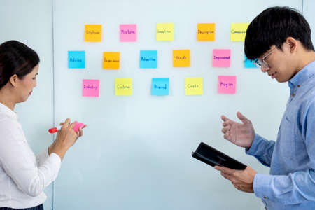 Businessmen and woman are standing He giving advice and brainstorming for Find an ideal and Write to notepad and stick it on the board.の写真素材
