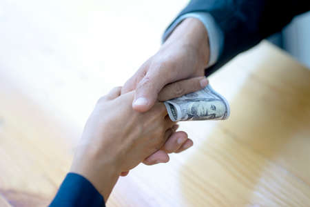 A businessman or official is accepting money handed over by a businessman while shaking hands secretly accepting bribes corruption concept.の写真素材
