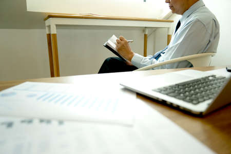 Smart businessman sitting happily thinking on a chair in the office  his hand hold the pen with more copy space.の写真素材