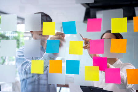 Businessmen and woman are standing He giving advice and brainstorming for Find an ideal and Write to notepad and stick it on the board.の写真素材