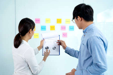 Businessmen and woman are standing He giving advice and brainstorming for Find an ideal and Write to notepad and stick it on the board.の写真素材