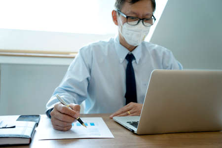 Smart businessman sitting happily thinking on a chair in the office  his hand hold the pen with more copy space.の写真素材