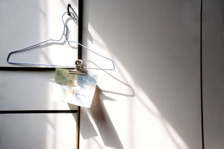 Thai banknotes are hung on hanger with paper clips on a shiny shadow white cabinet.の写真素材