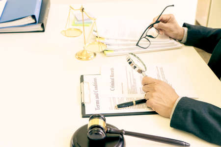 Lawyer or judge  was looking at the document with a magnifying glass to examine it thoroughly gavel on the table in law firm sepia vintage toneの写真素材