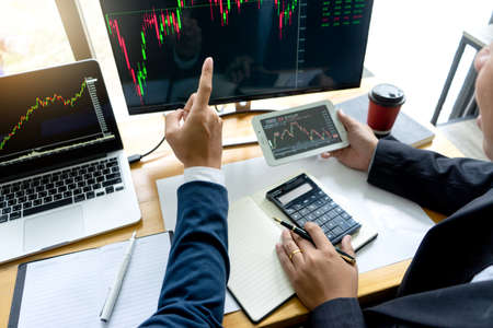 Businessmen are pointing to monitor to view stock market data on desktop computer and discuss it by analysis data from data graph.の写真素材