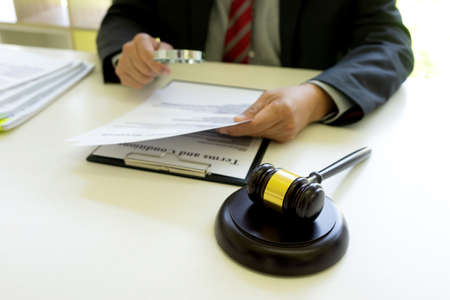 Lawyer or judge  was looking at the document with a magnifying glass to examine it thoroughly gavel on the table in law firm sepia vintage toneの写真素材
