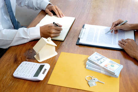Businessmen and clients are reading and signing contracts for buying or renting a house or real estate on a table with documents and house models.の写真素材