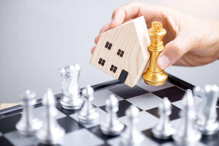 Hand hold  house model and gold king  chess in the surrounded by silver chess opponents.の写真素材