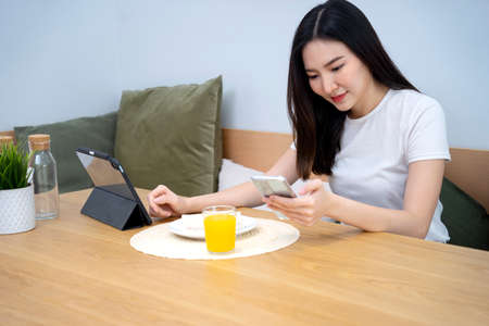 life style Morning women have breakfast  sandwiches  orange juice and follow the social world media via mobile phone and tablet happy smile with more copy space of wood tableの写真素材