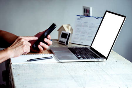 A businessman use mobile phone working from home on a white desk using a computer and pen paperの写真素材