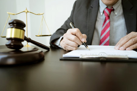 The lawyer was holding a pen to write legal documents on a table with a scale and a gavel in the law...