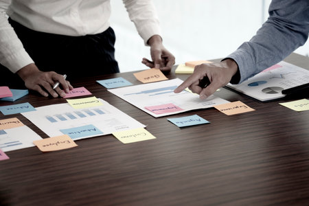 Two businessmen stand to consult with data graph chart paper and use color sticky notes to highlight information.の写真素材