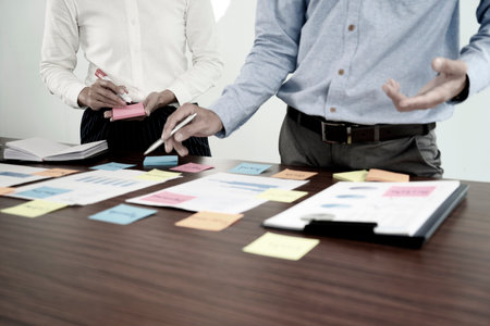 Two businessmen stand to consult with data graph chart paper and use color sticky notes to highlight information.の写真素材