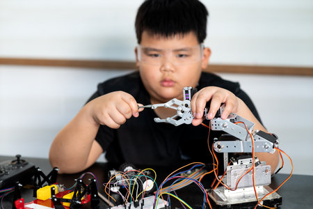 Asian boy is paying attention and adding and improving electronic parts to assemble new inventions...