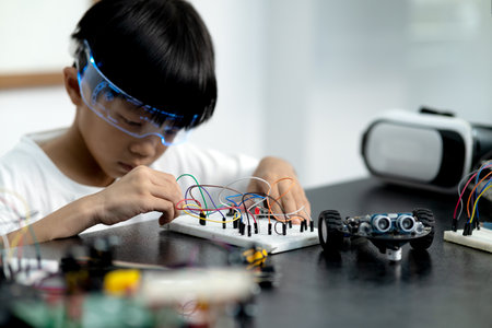 young boy having fun connecting electronic circuit board to connect with robot on the table for...