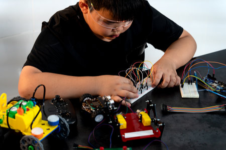 Asian boy is paying attention and adding and improving electronic parts to assemble new inventions...