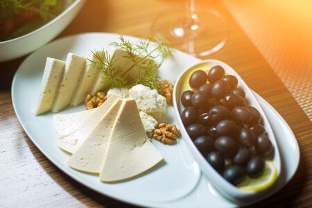 cheese plate with nuts, herbs and black olives on table.の写真素材