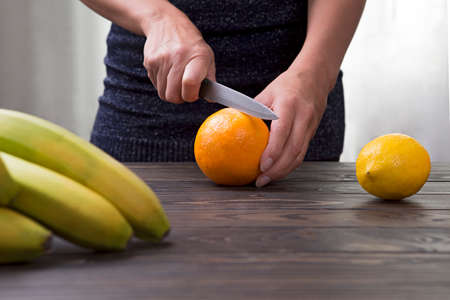 Woman cuts an orange with a knife.の写真素材
