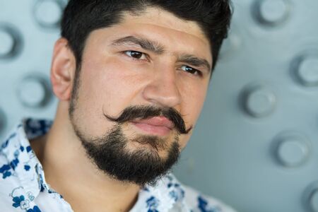 Portret of stylish bearded brunette guy. Young man posing on camera, dressed in light printed shirtの写真素材