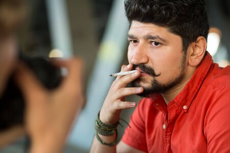 Brunette stylish bearded guy with a cigarette posing on camera. Backstage.
